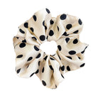 Cream-colored scrunchie with black polka dots held by a hand against a light background