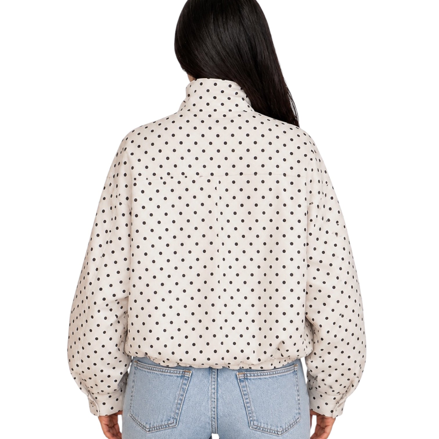 A woman viewed from the back wearing a cream-colored long-sleeve blouse with a black polka dot pattern and light-wash blue jeans, set against a plain white background.