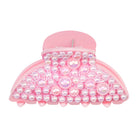 A pink hair claw clip embellished with iridescent pearls and rhinestones on a plain white background.
