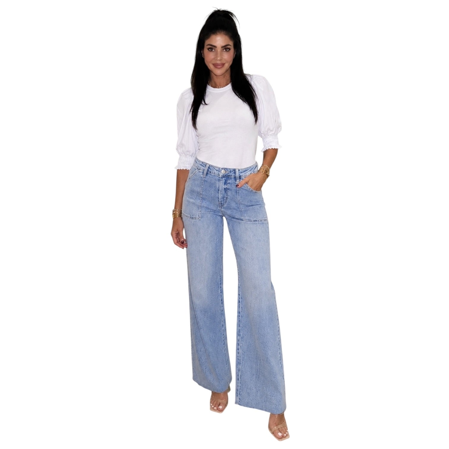 A woman modeling a pair of light-wash wide-leg denim jeans with a white puff-sleeve top, standing against a plain white background.