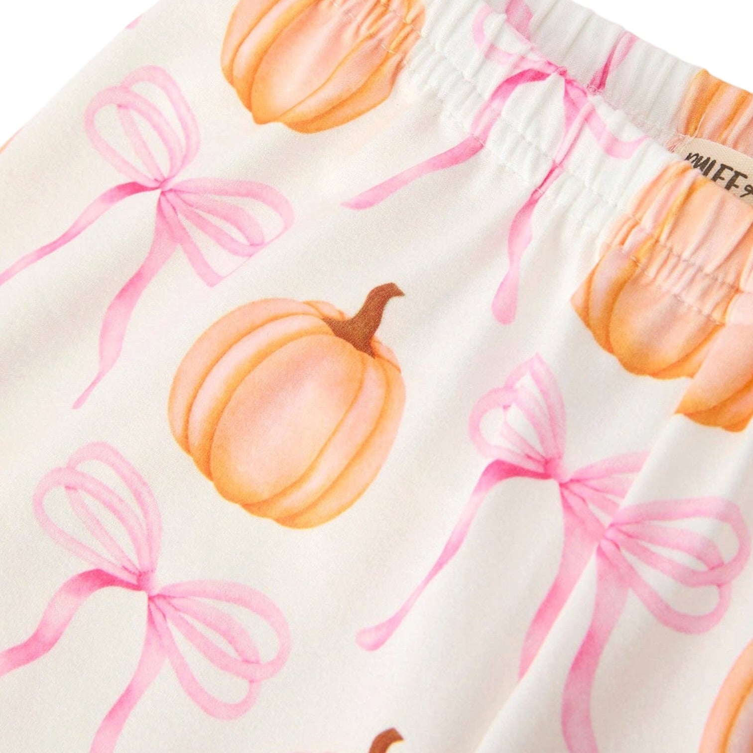 Close-up of a white fabric garment with a watercolor-style print of orange pumpkins and pink bows, showing an elastic waistband.