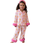 A young girl wearing a pink and orange pumpkin print pajama set with fluffy pink trim, including a long-sleeve top, matching pants, and a pink headband, shown against a plain white background.