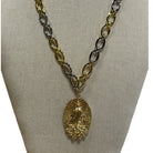 A gold and silver chain necklace with a textured gold pendant featuring an embossed religious figure, displayed on a beige fabric jewelry bust.