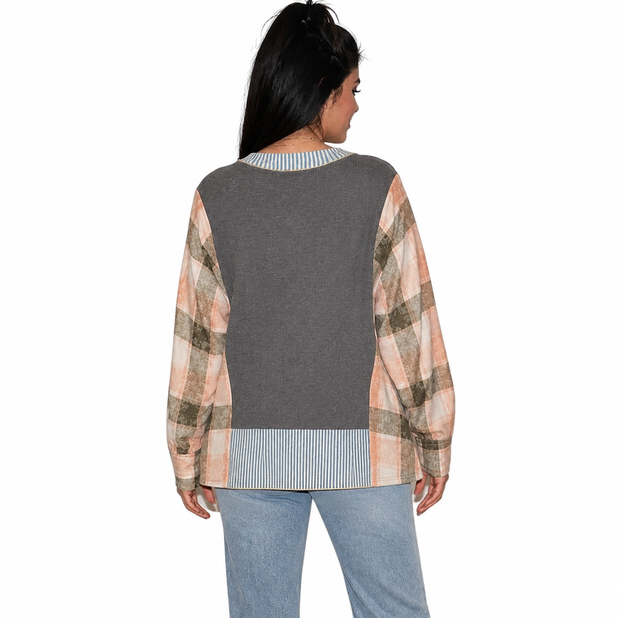 A woman shown from the back wearing a long-sleeve knit sweater with a solid dark gray back panel and peach, beige, and brown plaid sleeves, paired with light blue jeans against a white background.