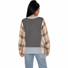 A woman shown from the back wearing a long-sleeve knit sweater with a solid dark gray back panel and peach, beige, and brown plaid sleeves, paired with light blue jeans against a white background.