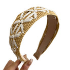 Hand holding a woven headband with beige and white colors against a neutral background