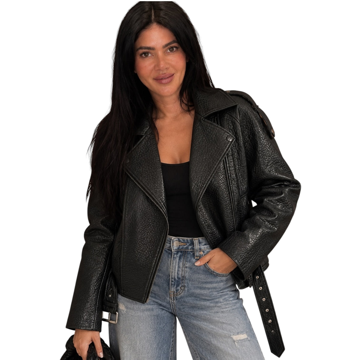A woman wearing a black textured faux-leather moto jacket with a belted waist, styled with a black top and light-wash distressed jeans, against a plain white background.