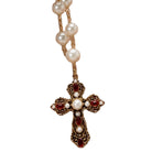 An ornate cross pendant necklace featuring a gold-toned filigree design with red gemstone accents and white faux pearls, shown against a plain white background.