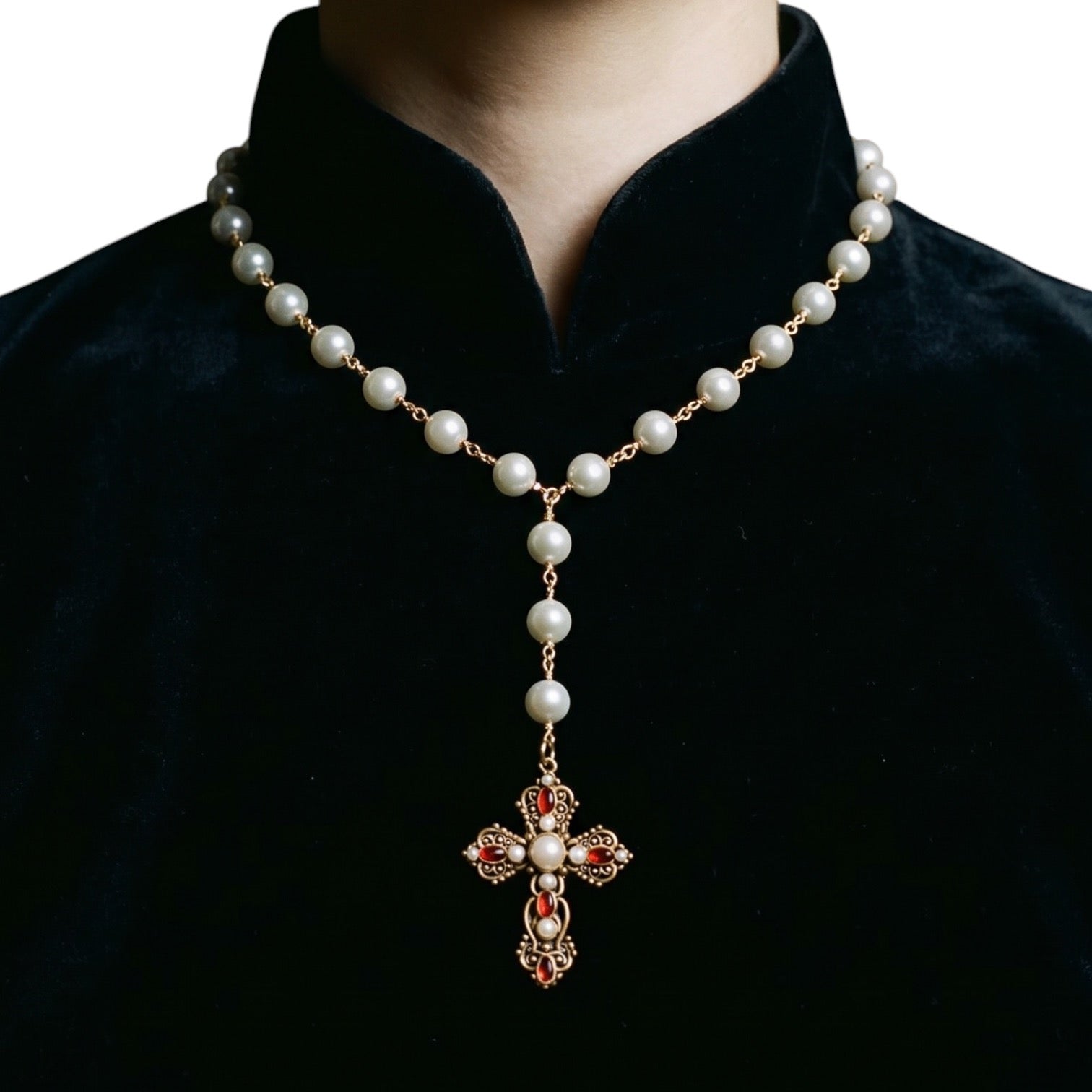 A pearl and gold cross necklace with red gemstone accents, shown worn on a person's neck over a black velvet collar.