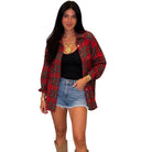 A woman modeling a red and black plaid flannel shirt over a black tank top and denim shorts, standing against a plain white background.