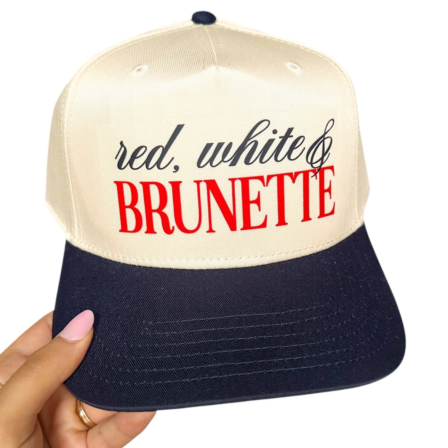 Cap with 'red, white & BRUNETTE' text held by a hand on a white background