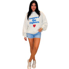 A woman modeling a white sweatshirt with blue and red text reading 'Support the Fighters' and a red heart, paired with denim shorts and white sneakers on a plain white background.