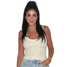 A woman with long dark hair wearing a fitted off-white ribbed tank top and light blue jeans, standing against a plain white background.