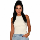 A woman with long black hair wearing a fitted cream-colored sleeveless mock neck top and light blue jeans, standing against a solid white background.
