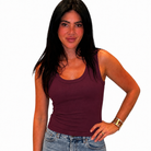 A woman modeling a sleeveless scoop-neck tank top in deep burgundy, paired with light-wash blue jeans, against a plain white background.