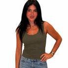 A woman with long black hair wearing a fitted olive green tank top and light blue jeans, standing against a plain white background.