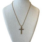 A gold-tone cross pendant necklace with small clear rhinestones, displayed on a cream-colored fabric mannequin bust against a white background.