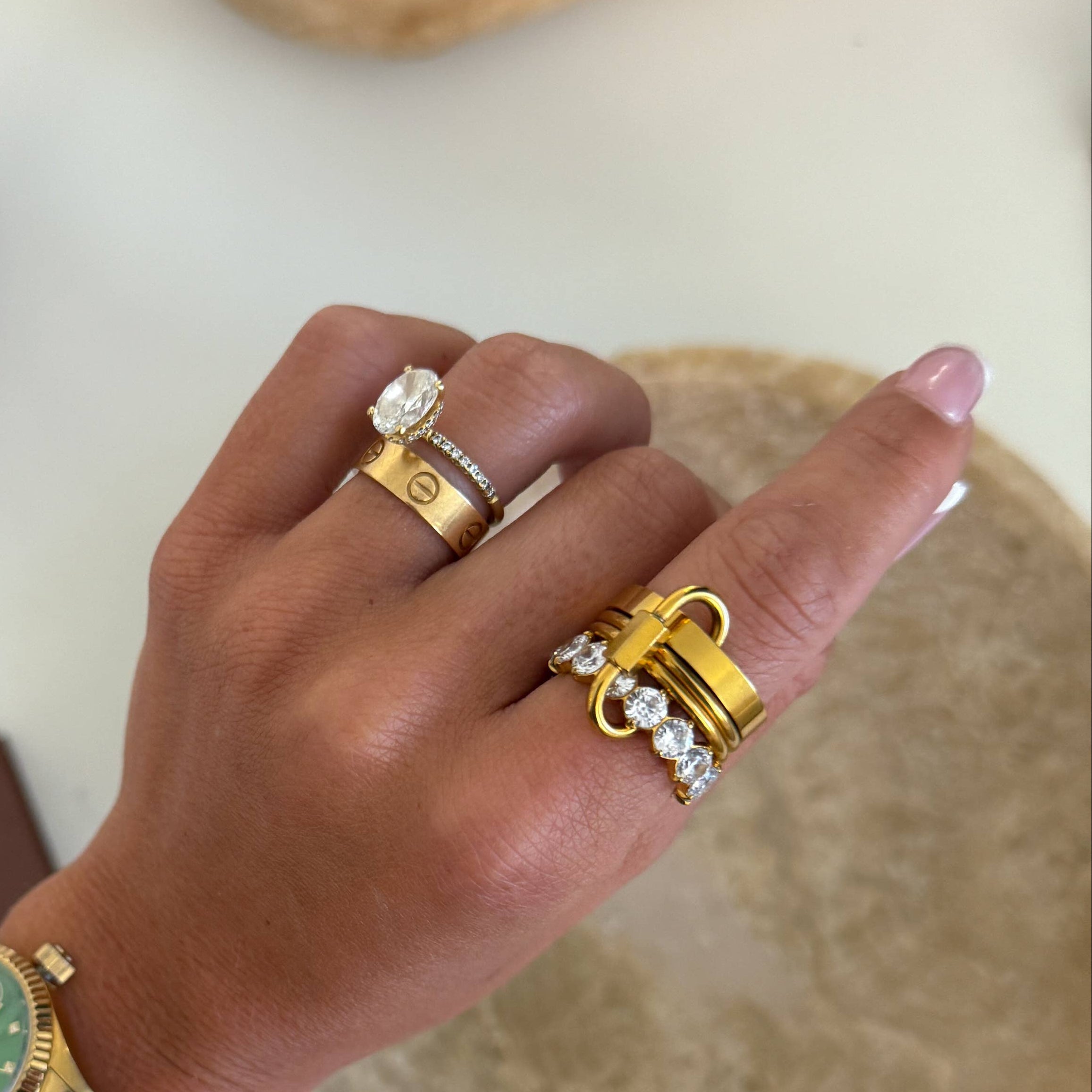 Hand wearing gold rings with gemstones on a neutral background