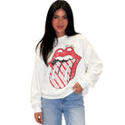 A woman modeling a white crewneck sweatshirt featuring a large, striped red and white Rolling Stones lips graphic on the front, paired with light blue jeans against a plain white background.