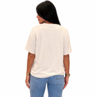 A woman viewed from the back wearing an oversized off-white t-shirt and light blue jeans, set against a plain white background.