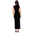 A woman viewed from the back wearing a sleeveless black velvet maxi dress with a draped neckline and gathered side detail, paired with black high heels, on a plain white background.