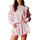 Woman wearing a pink floral lounge set with ruffled details on a white background