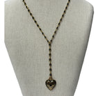 A long gold-toned beaded necklace with a heart-shaped pendant, displayed on a neutral fabric jewelry bust against a white background.