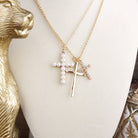 Gold necklace with cross pendant and pearl accents on a white surface.