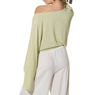 Woman wearing a light green off-shoulder top and white pants on a white background