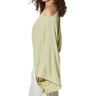 Woman wearing a light green off-shoulder top and white pants on a white background