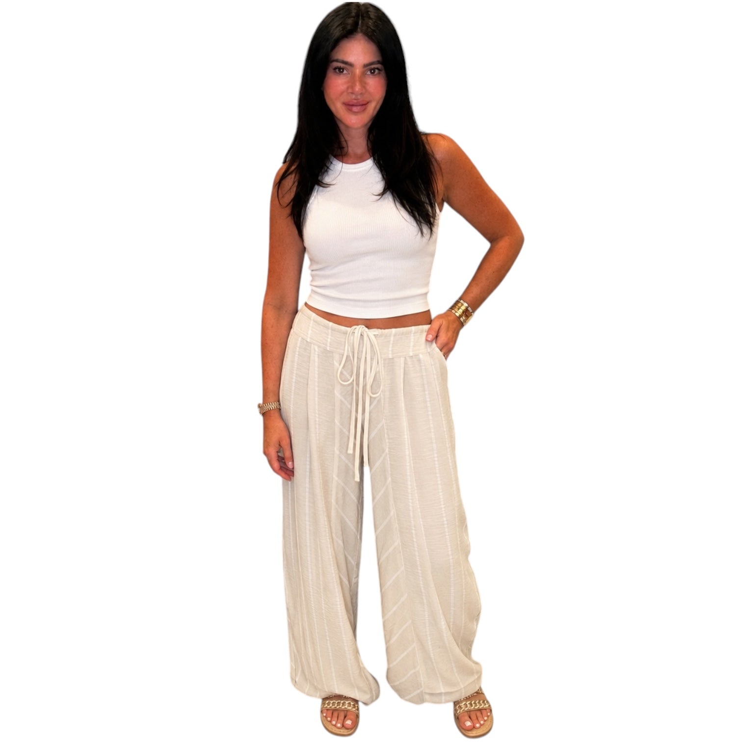 Woman wearing a white sleeveless top and beige wide-leg pants on a white background