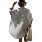 Person wearing a white shirt with an eye design and holding a straw bag on a white background