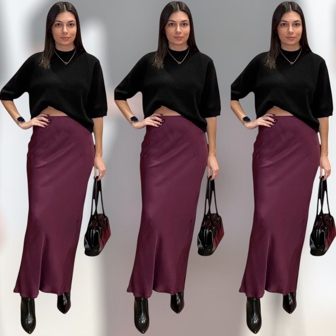 Woman wearing a black top and burgundy skirt with a black handbag on a gray background