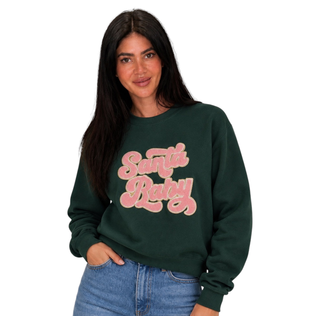 A woman wearing a dark forest green crewneck sweatshirt with 'Santa Baby' printed in a pink retro bubble font across the chest, paired with blue jeans against a plain white background.