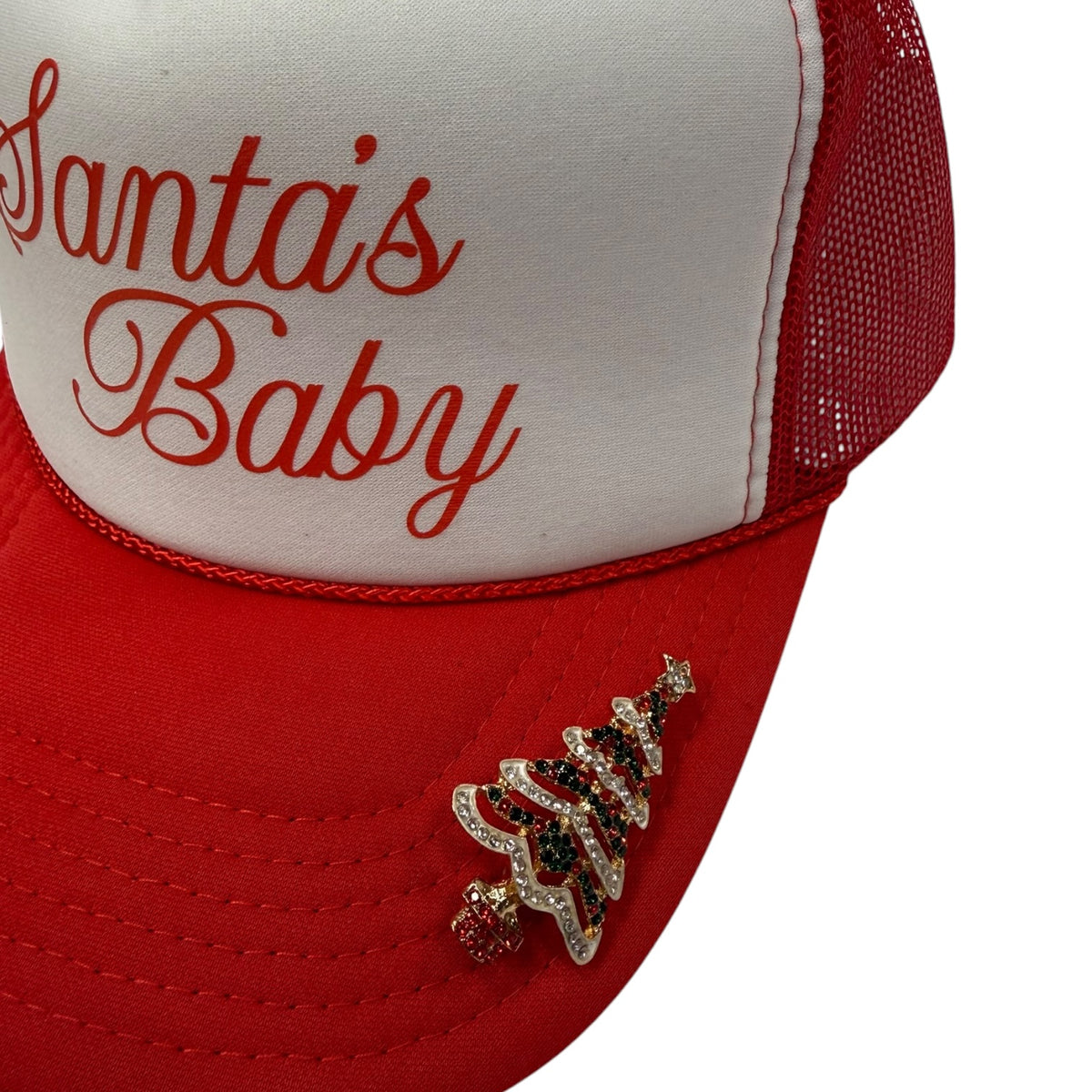 A close-up of a red and white trucker hat with 'Santa's Baby' embroidered in red script on the white front panel. The red mesh back and curved brim are also red.