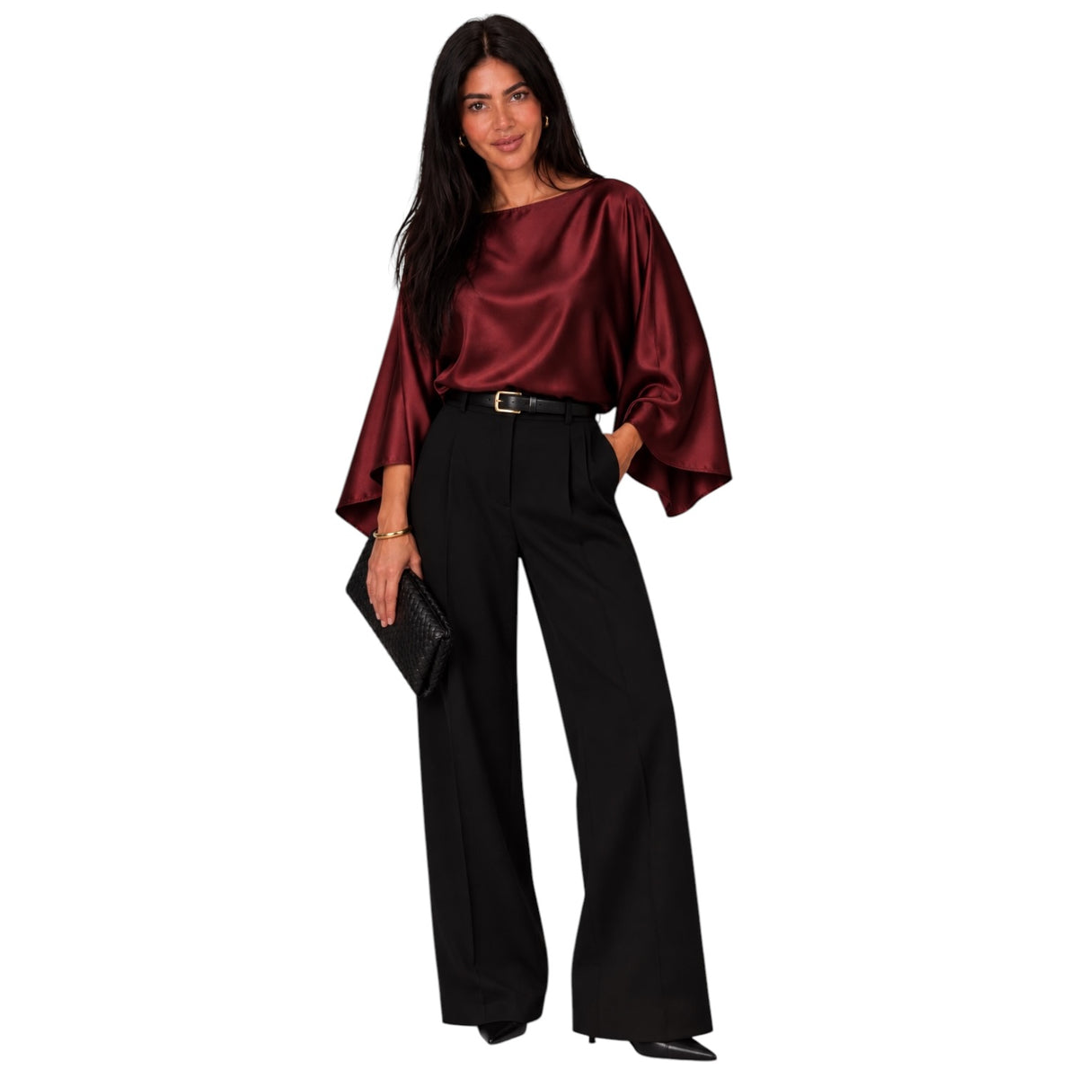 A woman modeling a satin-like burgundy top with dramatic wide sleeves and black wide-leg trousers, holding a black clutch against a plain white background.