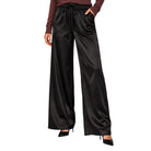 Black wide-leg satin pants with an elastic drawstring waist, modeled with a brown long-sleeve top and black heels on a white background.