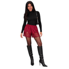A woman modeling a black long-sleeve mock neck top, burgundy lace-trimmed shorts, sheer black tights, and black knee-high boots, with a small black shoulder bag, against a plain white background.