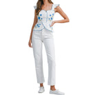 Woman wearing a white top with blue floral embroidery and white pants on a white background