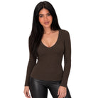 A woman modeling a fitted, long-sleeve V-neck top in dark brown, paired with black faux-leather pants, against a solid white background.
