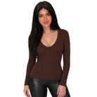A woman modeling a fitted, long-sleeve brown V-neck top with black faux-leather pants against a plain white background.