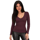 A woman modeling a long-sleeve, scoop-neck ribbed knit top in a deep plum purple color, paired with black faux-leather pants, against a solid white background.