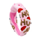 A pink knotted fabric headband decorated with red and white Santa hat embellishments, gold beaded letters spelling 'HO HO HO', and small rhinestone accents, shown on a plain white background.