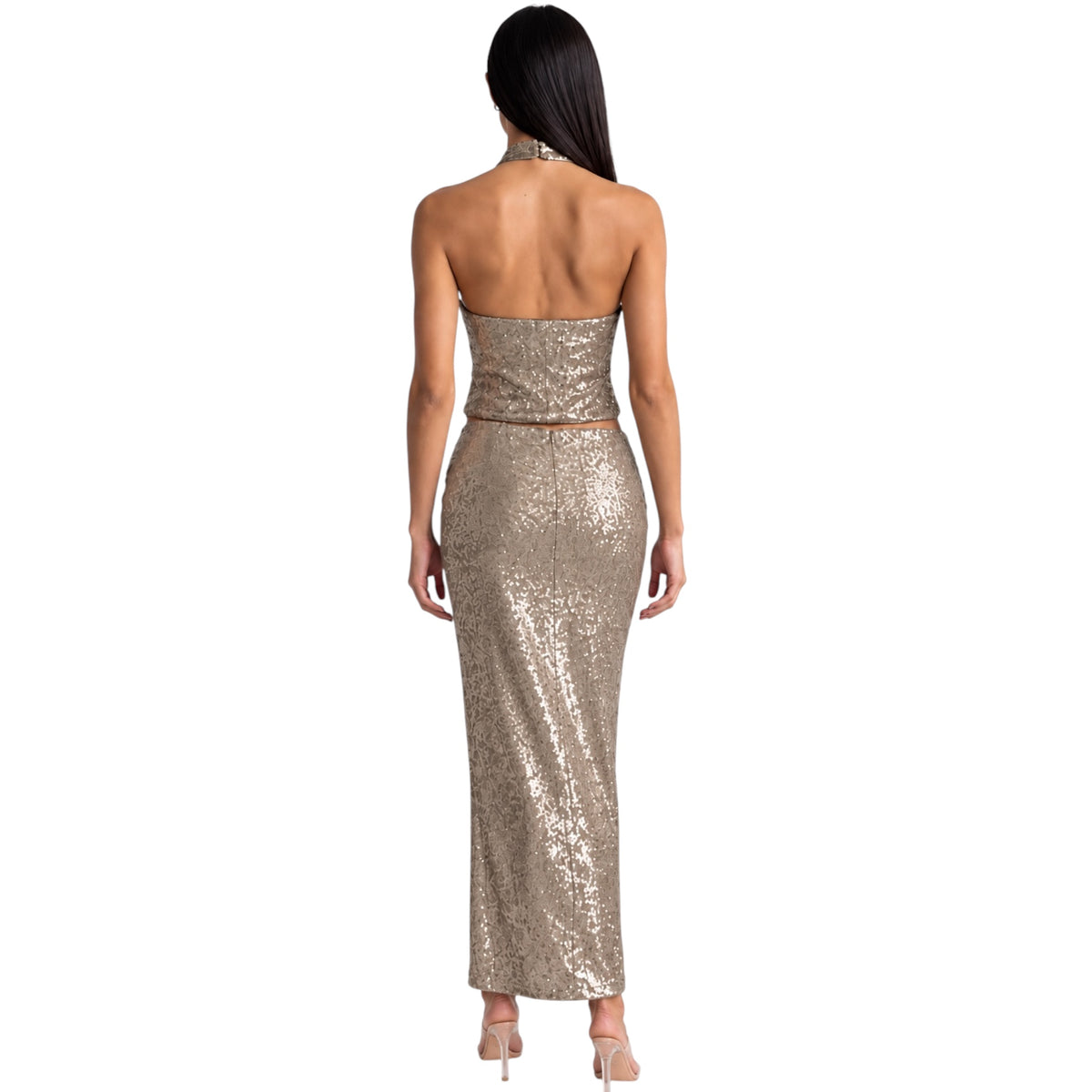 A woman shown from the back wearing a strapless, sequined halter maxi dress in a metallic champagne gold color, paired with nude high heels, against a plain white background.