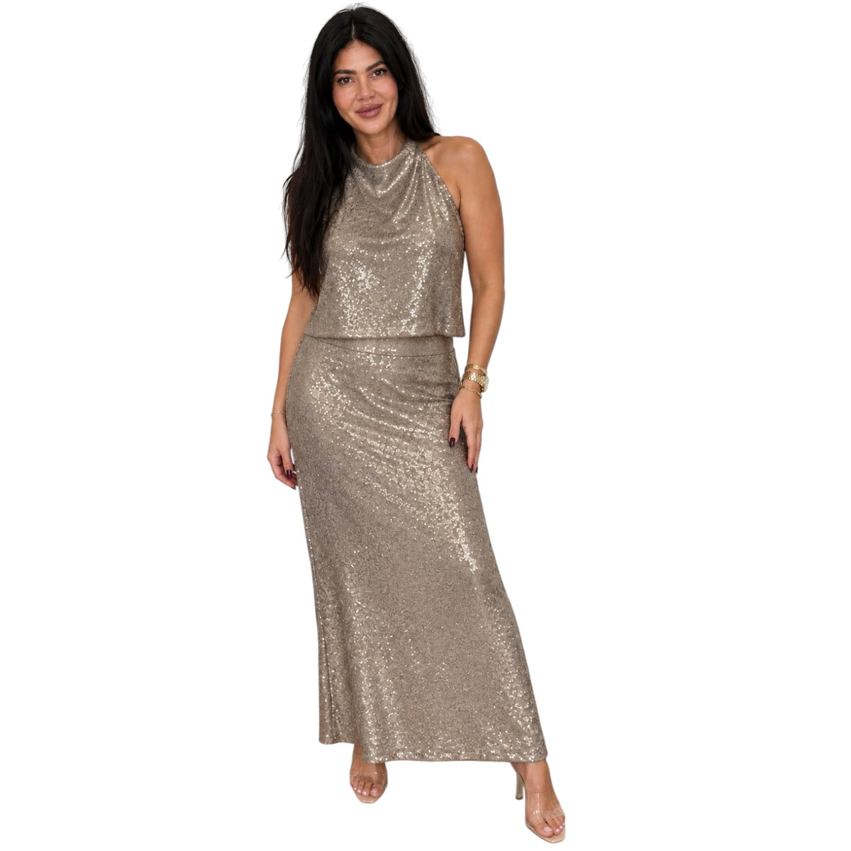 A woman modeling a sleeveless, high-neck, two-piece sequin set in a champagne gold color, consisting of a cropped top and a matching maxi skirt, against a plain white background.
