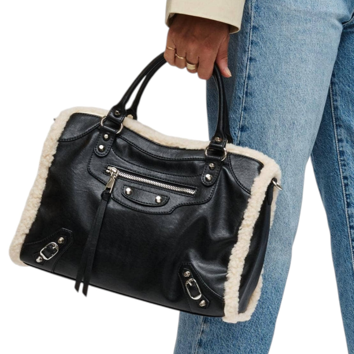 A black leather handbag with a cream shearling lining, held by a person wearing blue jeans and a light beige jacket against a white background.