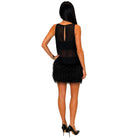 A woman shown from the back wearing a black sleeveless dress with a sheer mesh back panel and a short black feathered skirt, paired with black high heels, against a plain white background.