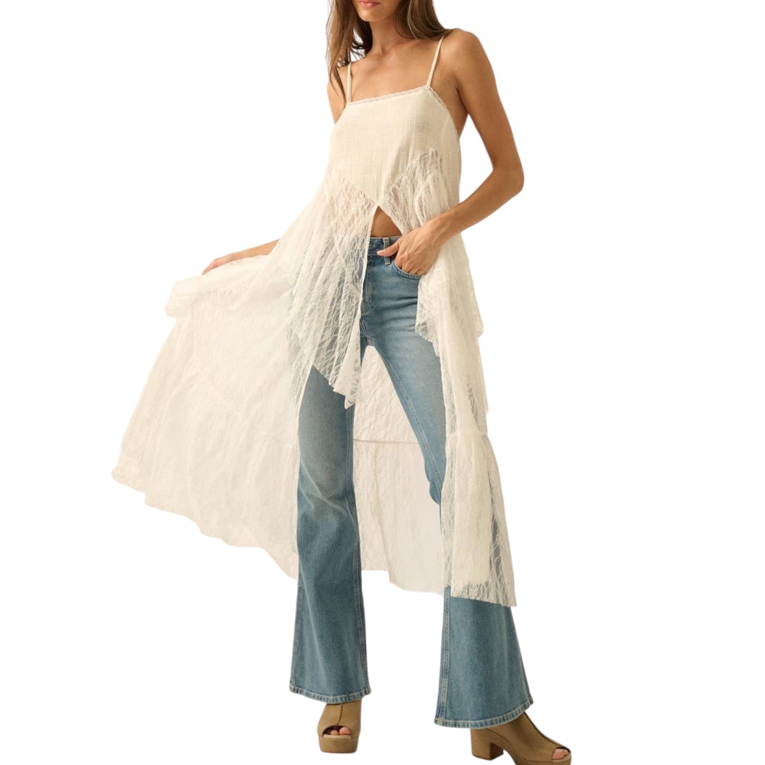 Woman wearing a white lace cover-up over a swimsuit with blue jeans on a white background
