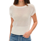 Woman wearing a beige knit top and blue jeans on a white background