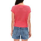 Person wearing a pink textured top and denim shorts on a white background